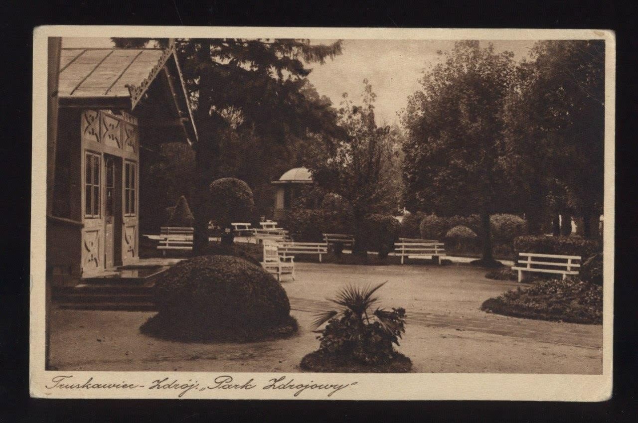 Куточок курортного парку Трускавця на листівці 1920-х: різьблений дерев'яний павільйон, білі лави, стрижені кущі