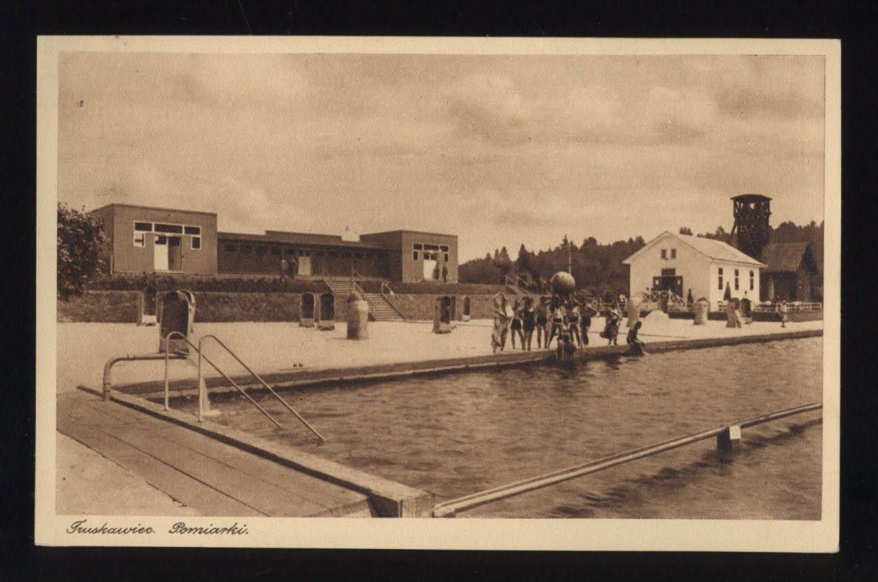 Відкритий басейн у Поміарках Трускавця: купальники біля води, модернові купальні корпуси та вишка соляної копальні на задньому плані