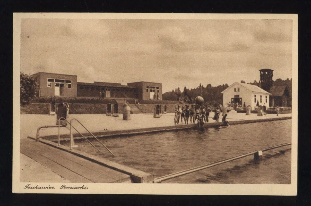 Відкритий басейн у Поміарках Трускавця: купальники біля води, модернові купальні корпуси та вишка соляної копальні на задньому плані