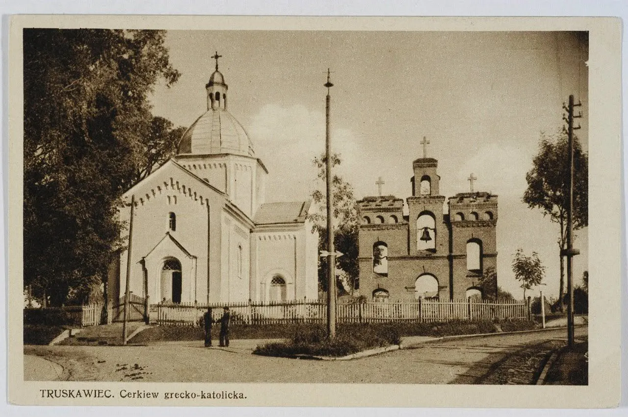 Церква святого Миколая у Трускавці на сепійній листівці: білий мурований храм з банею, цегляна дзвіниця та дві постаті біля паркану
