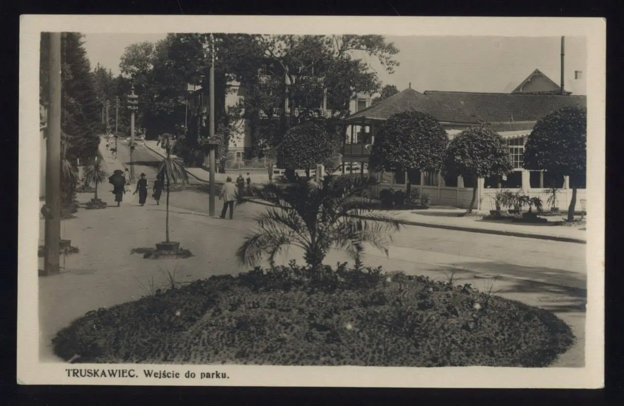 Вхід до курортного парку Трускавця на листівці 1930-х: кругла клумба з пальмою, стрижені туї, павільйон із верандою