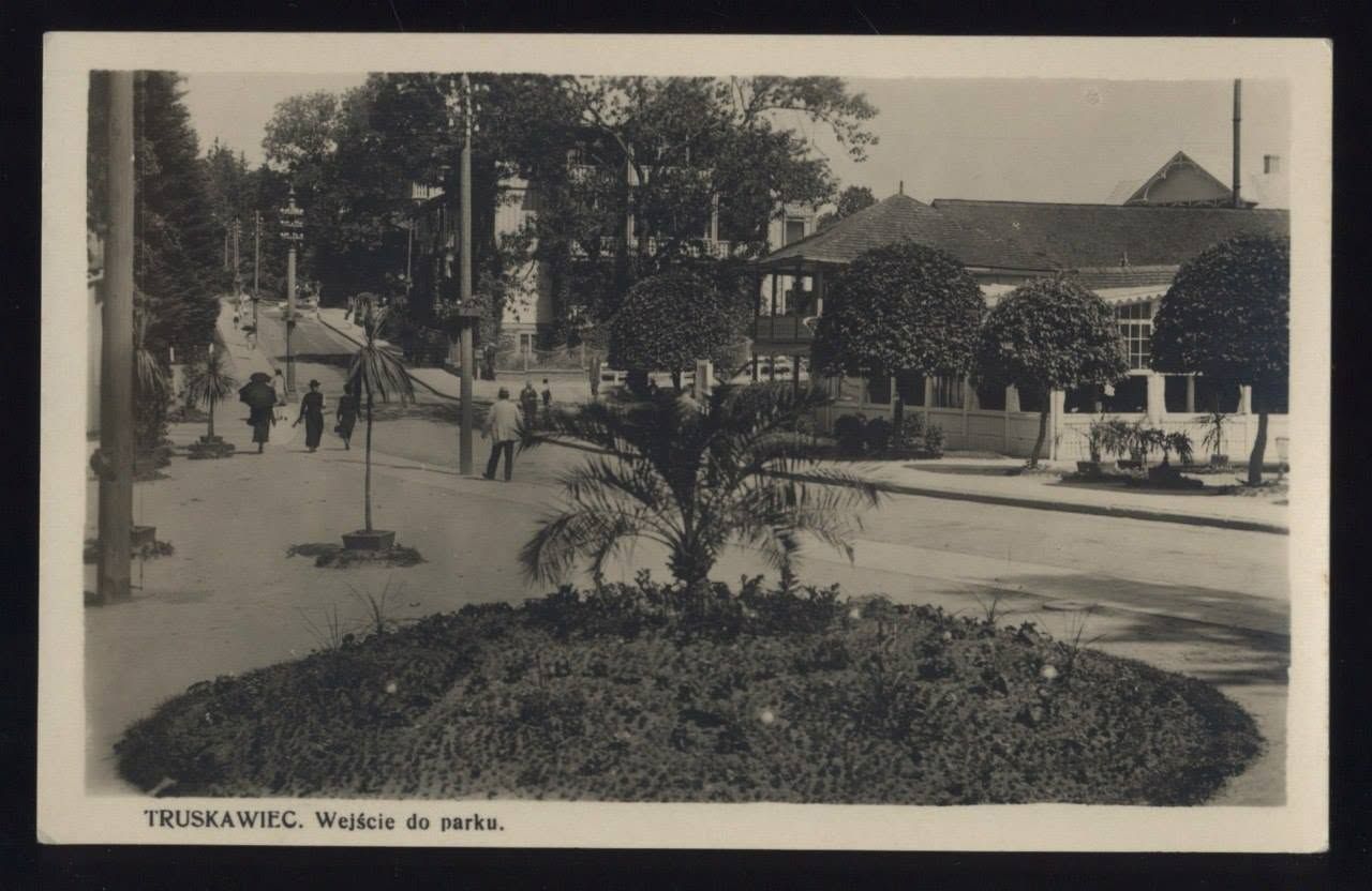 Вхід до курортного парку Трускавця на листівці 1930-х: кругла клумба з пальмою, стрижені туї, павільйон із верандою